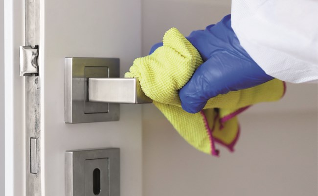 Eine Türklinke wird händisch mit Desinfektionsmittel gereinigt.