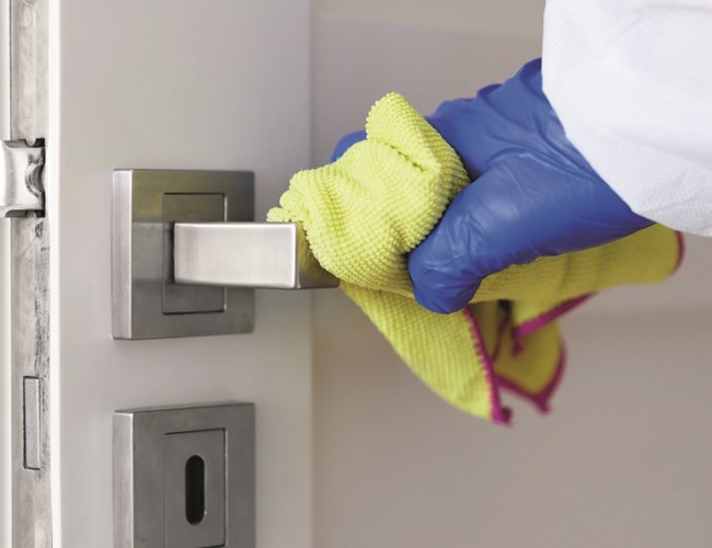 Eine Türklinke wird händisch mit Desinfektionsmittel gereinigt.